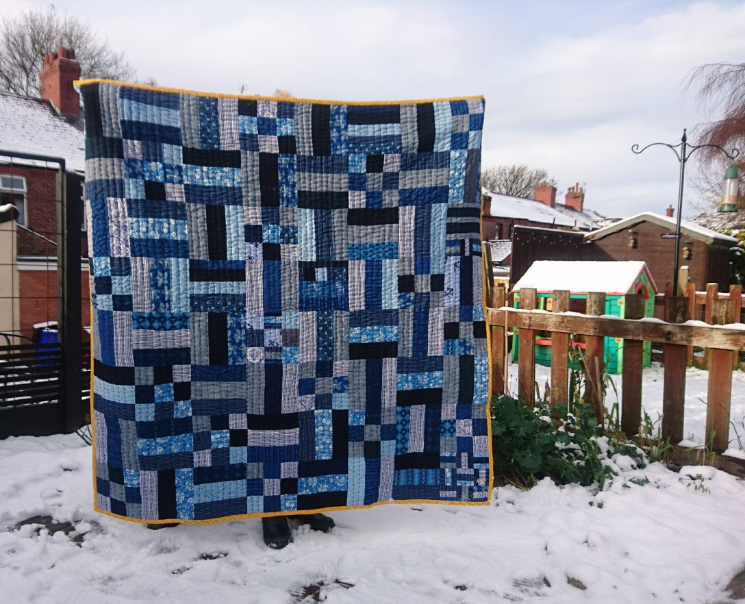 a blue rail fence quilt is held up in a snowy garden